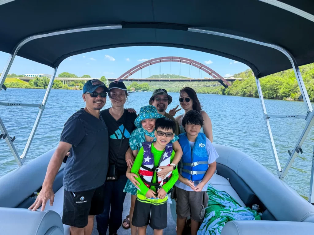 A happy family on a Wake Riderz private boat tour cruising towards the iconic 360 Bridge on Lake Austin during the day. 