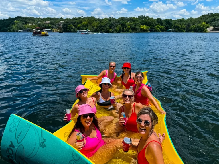 Women in pink hats celebrating on a floating pad during a captained Lake Austin boat tou