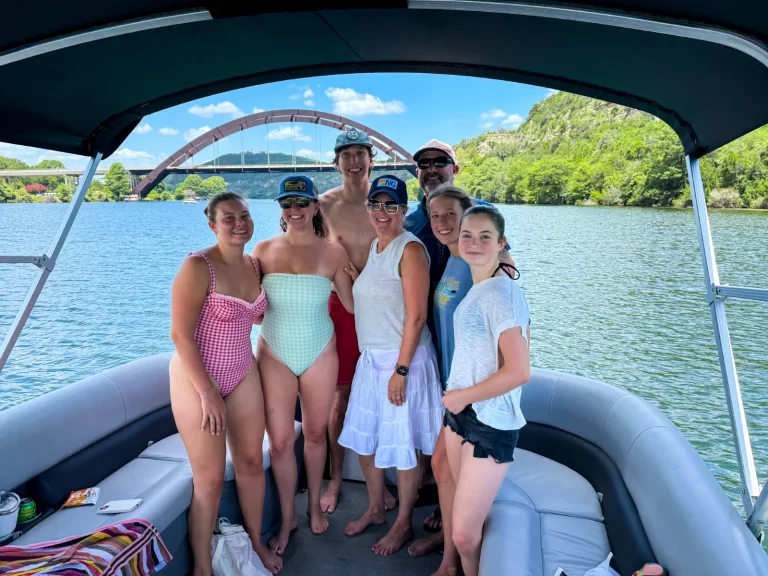 Family smiling together on a captained pontoon boat with the Pennybacker Bridge in the background on Lake Austin
