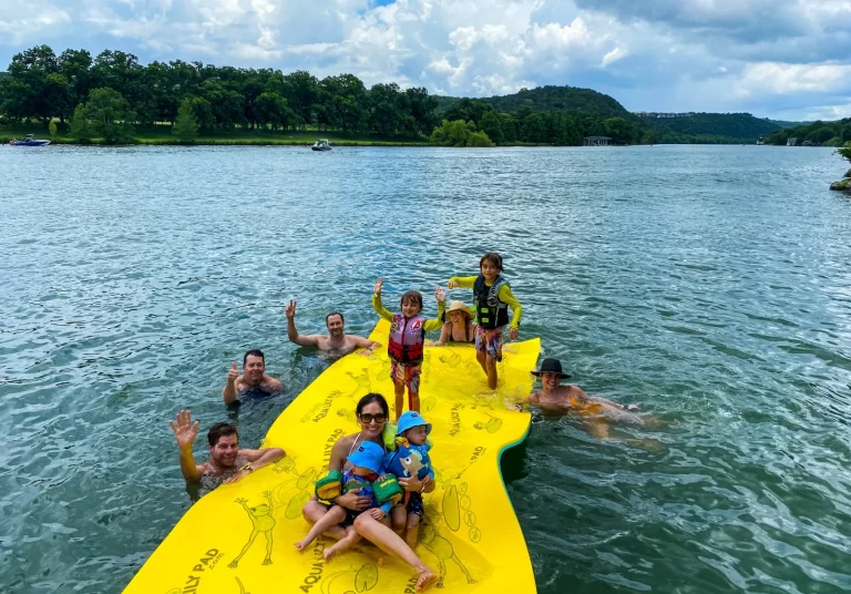 Family and friends enjoying a fun Lake Austin boat day while relaxing and playing on a large floating pad
