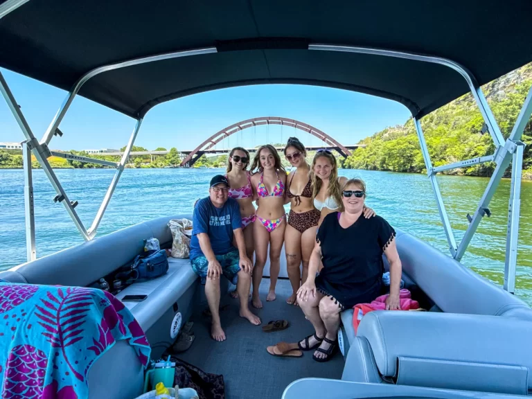 Family and friends posing on a captained pontoon boat with the Pennybacker Bridge in view on Lake Austin