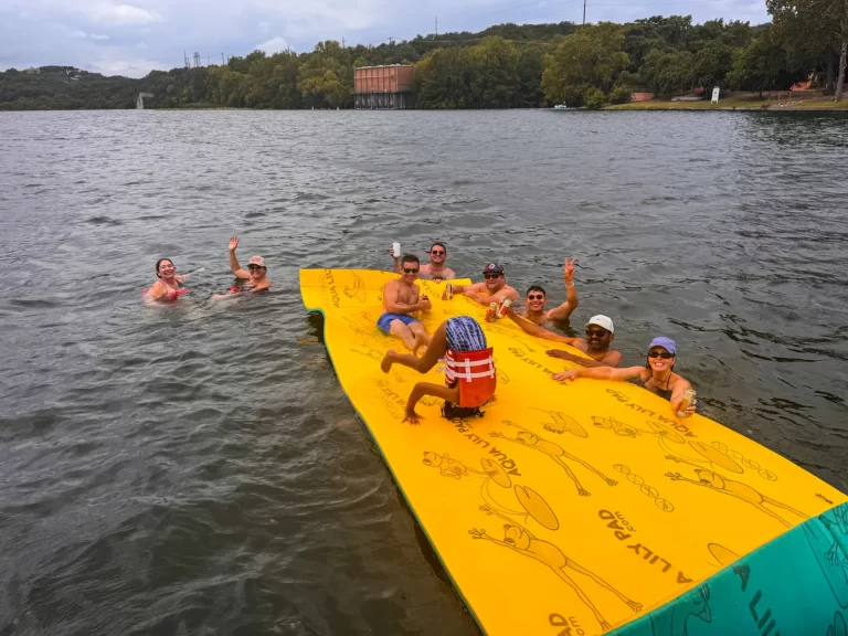 Group of friends waving and relaxing on a floating pad during a Lake Austin party boat rental