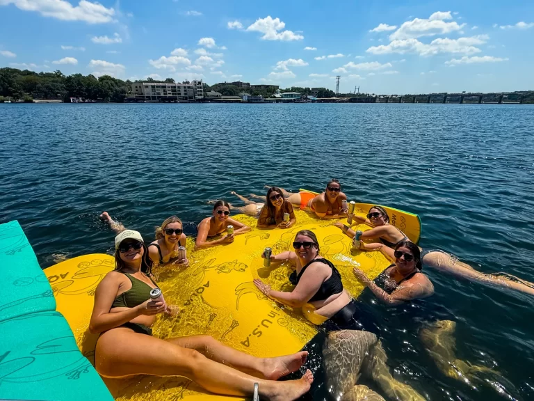 Group of women enjoying drinks and sunshine on a large floating pad during a Lake Austin boat party