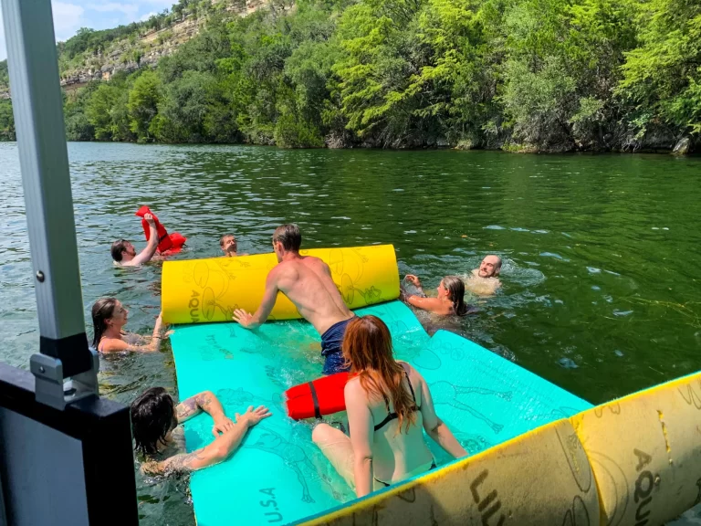 Group swimming and playing around a floating pad during a Lake Austin boat rental