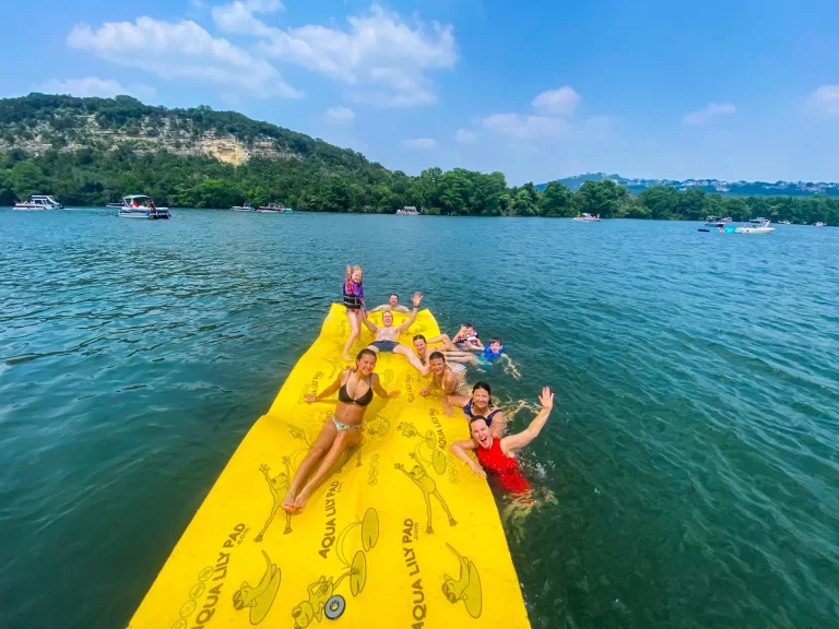Group relaxing and waving from a floating pad during a sunny Lake Austin captained boat rental