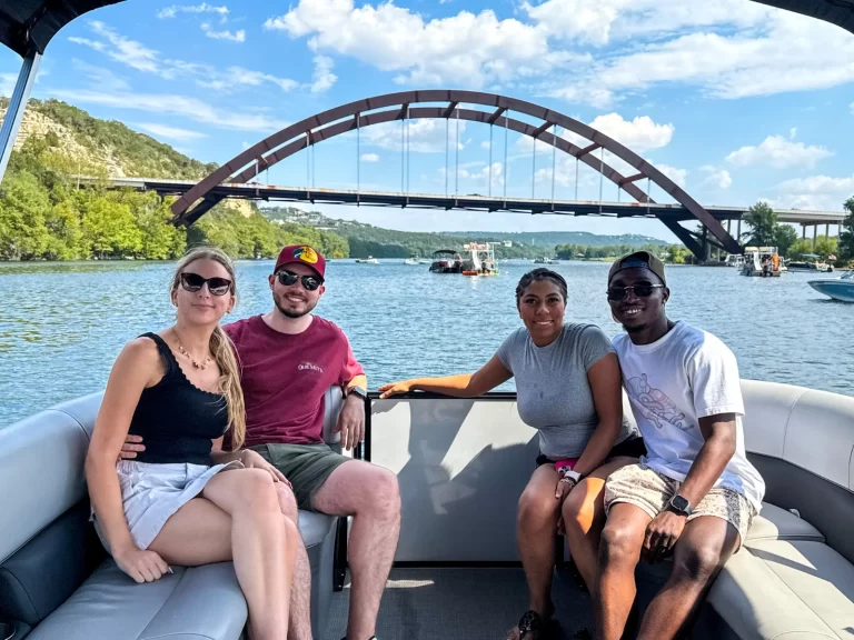Four friends enjoying a Lake Austin pontoon boat tour with a clear view of the Pennybacker Bridge behind them