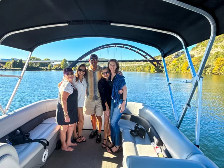 Group posing on a captained pontoon boat on Lake Austin with the Pennybacker Bridge and fall colors behind them