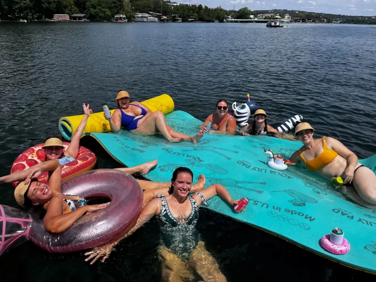 Women enjoying a sunny Lake Austin boat day while relaxing on a floating pad with drinks