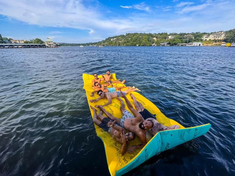 Group of friends relaxing on a floating pad during a sunny Lake Austin captained boat outing