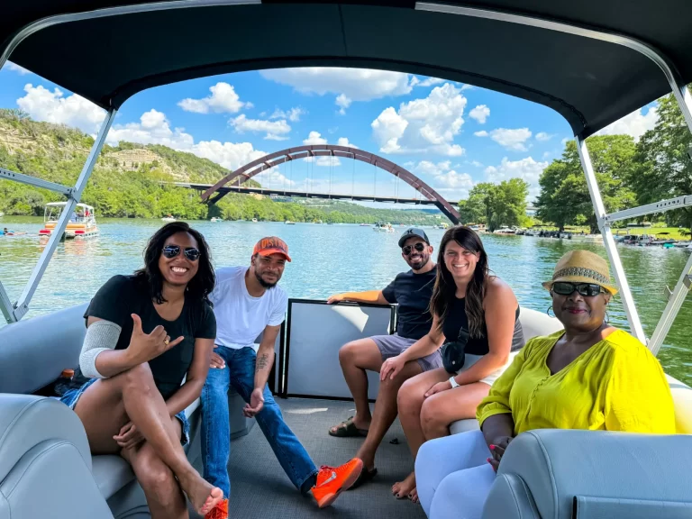 Group of friends enjoying a captained pontoon tour on Lake Austin with the Pennybacker Bridge behind them